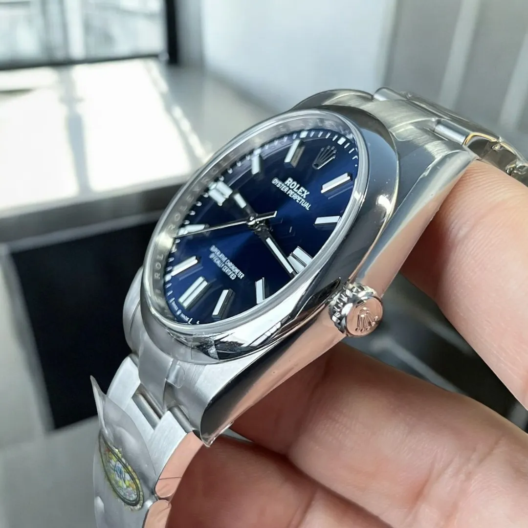 Replica Rolex Oyster Perpetual Blue Dial watch shown at a 45-degree angle, showcasing the fine details of the Oystersteel case and the prominent crown design.