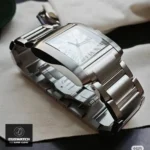 Luxury stainless steel super clone timepiece laid flat, displaying 33.7mm x 25.5mm Tank Francaise case dimensions on wooden surface