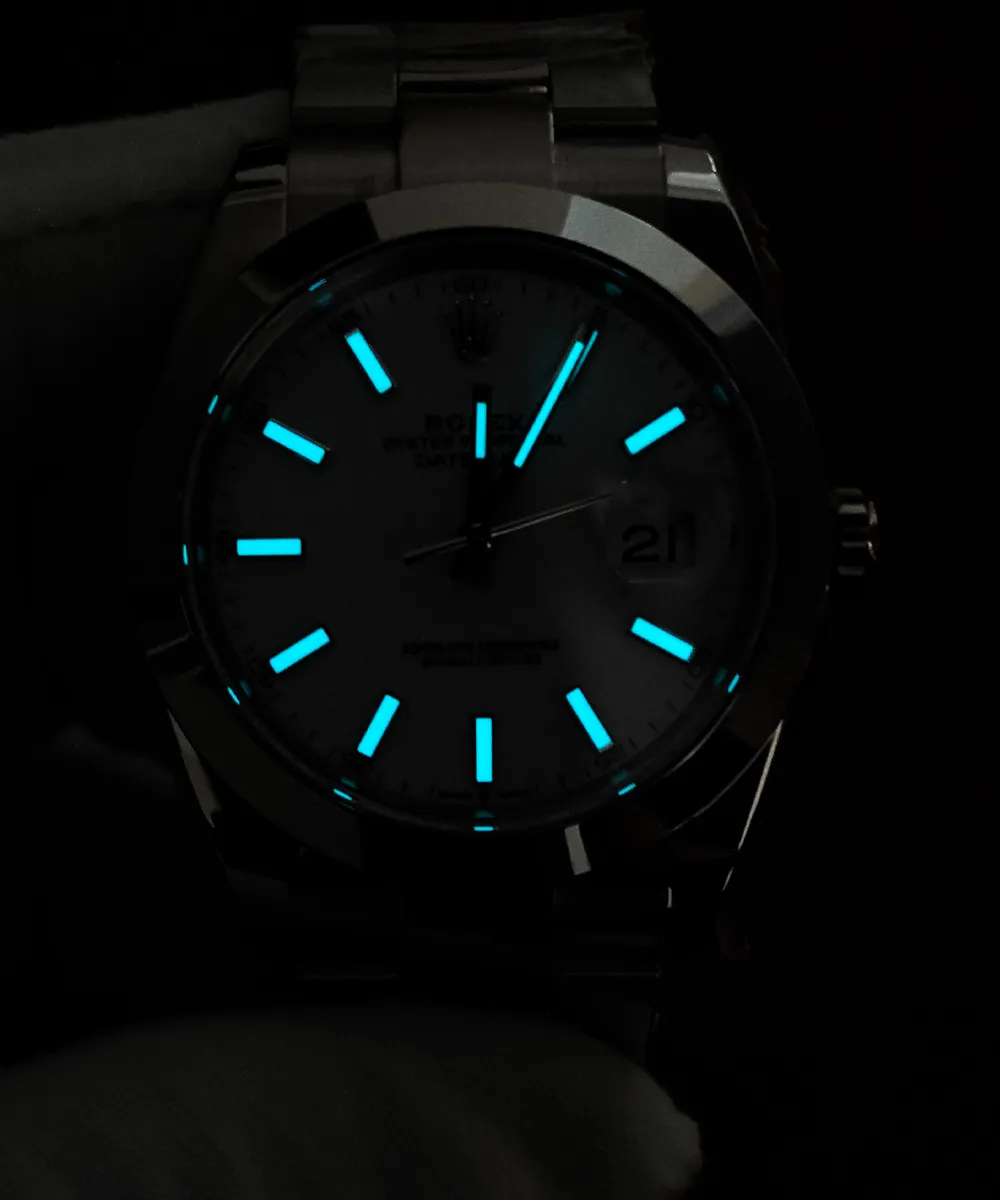 Rolex Datejust 126300 in darkness, showing blue luminescent hour markers and hands against the white dial.